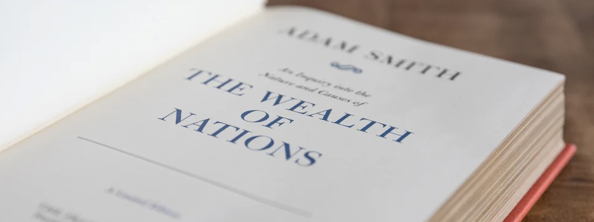 An open copy of The Wealth of Nations by Adam Smith, showing the title page, resting on a wooden surface.