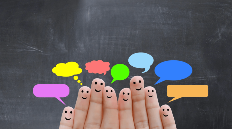 Six fingers with smiley faces drawn on them, each paired with a different colored speech bubble, in front of a dark chalkboard.