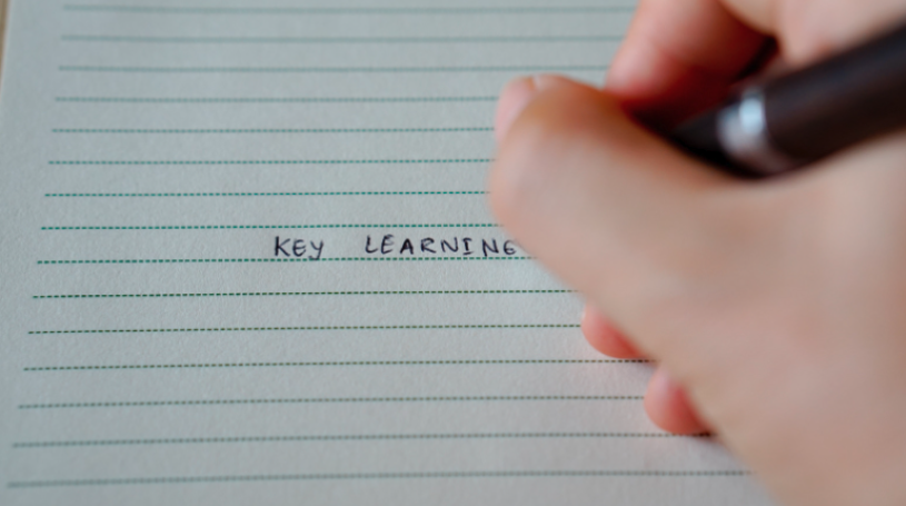 A hand writes the words Key Learning in pen on a sheet of lined notebook paper..