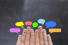 Six fingers with smiley faces drawn on them, each paired with a different colored speech bubble, in front of a dark chalkboard.