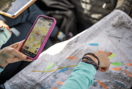  A person points at a paper topographic map marked with colored highlighter while holding a phone that shows the same terrain in a digital mapping app. Image: Garth Milan