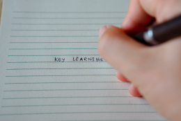 A hand writes the words Key Learning in pen on a sheet of lined notebook paper.
