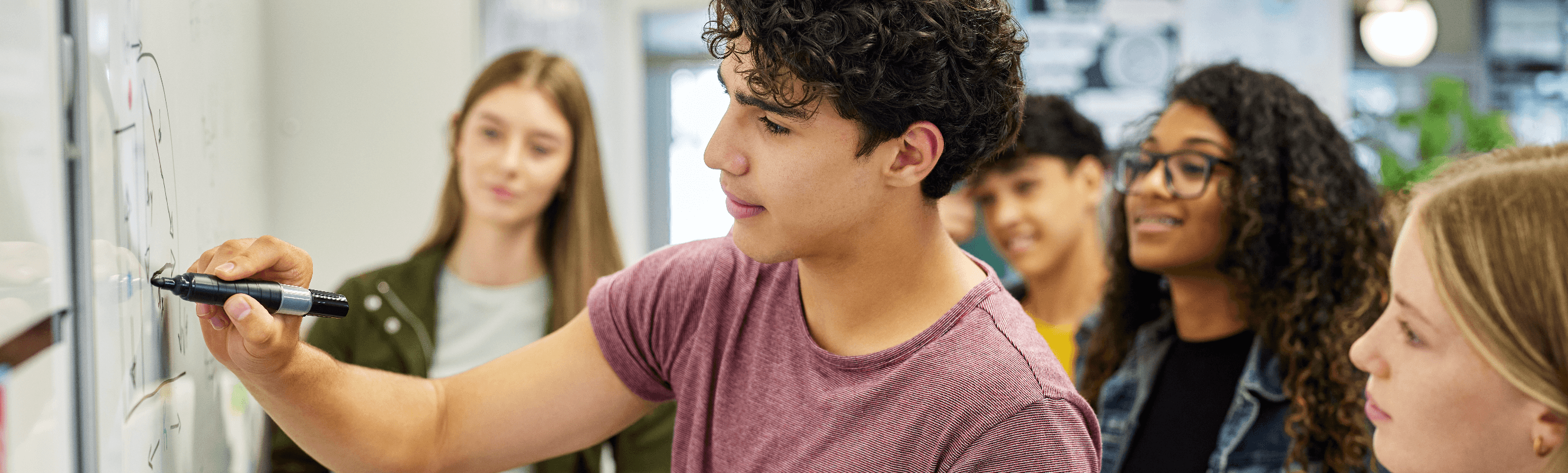 Students stand around a whiteboard while one fills out an economics problem with the class.