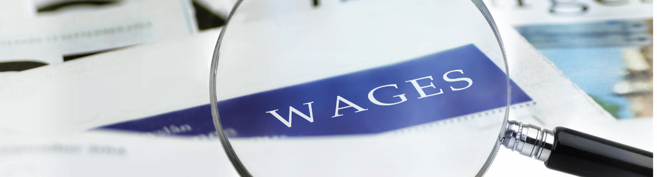 A magnifying glass focusing on the word "WAGES" printed on a document, with other papers blurred in the background.