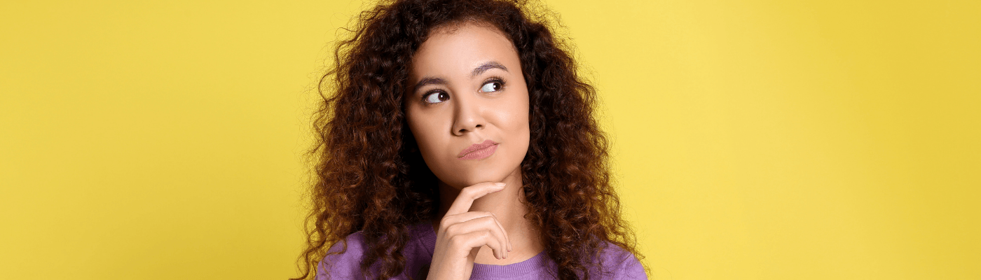 A woman stands against a yellow background in a contemplative stance.