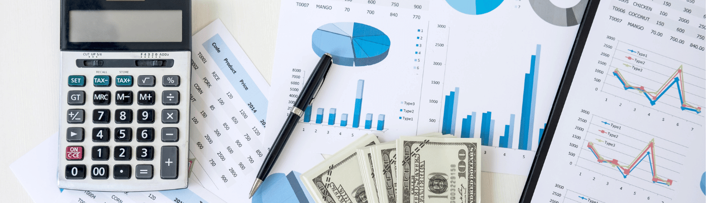 A calculator, pen, dollar bills, and charts with bar and line graphs spread across a desk, representing the analysis of macroeconomic indicators — GDP, unemployment, and inflation — covered in this lesson.