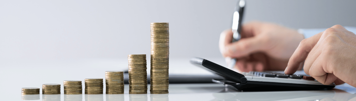 Stacks of coins arranged in ascending height beside a person using a calculator and pen, representing the role of interest rates in connecting borrowers and savers through commercial banks.