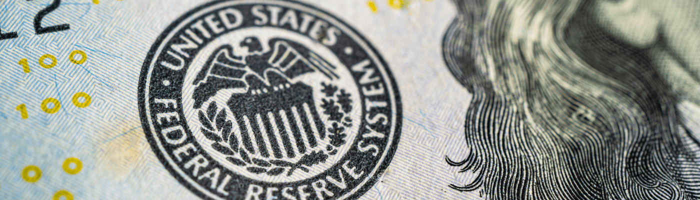 A close-up of the Federal Reserve System seal printed on a U.S. dollar bill, representing the Federal Reserve's role in setting the federal funds rate and conducting monetary policy.