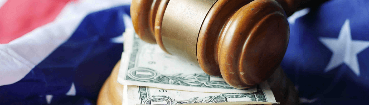 A wooden gavel rests on U.S. dollar bills draped over an American flag, representing the role of Congress and the president in setting fiscal policy through taxation and spending decisions.