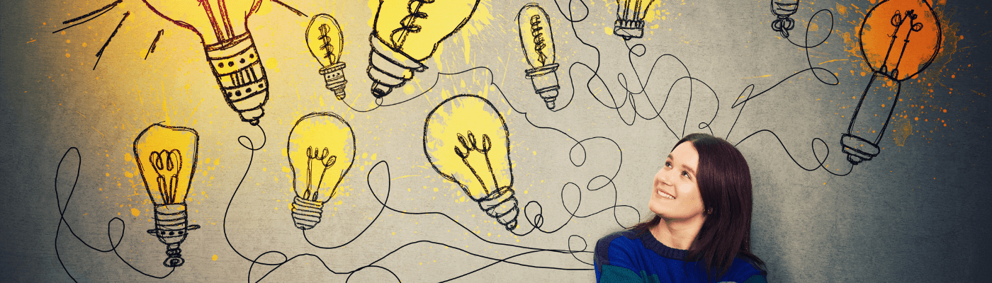 A young woman smiles and looks upward at a wall covered in illustrated light bulbs connected by tangled lines, representing the exploration of economic indicators beyond the "Big 3" in this lesson.