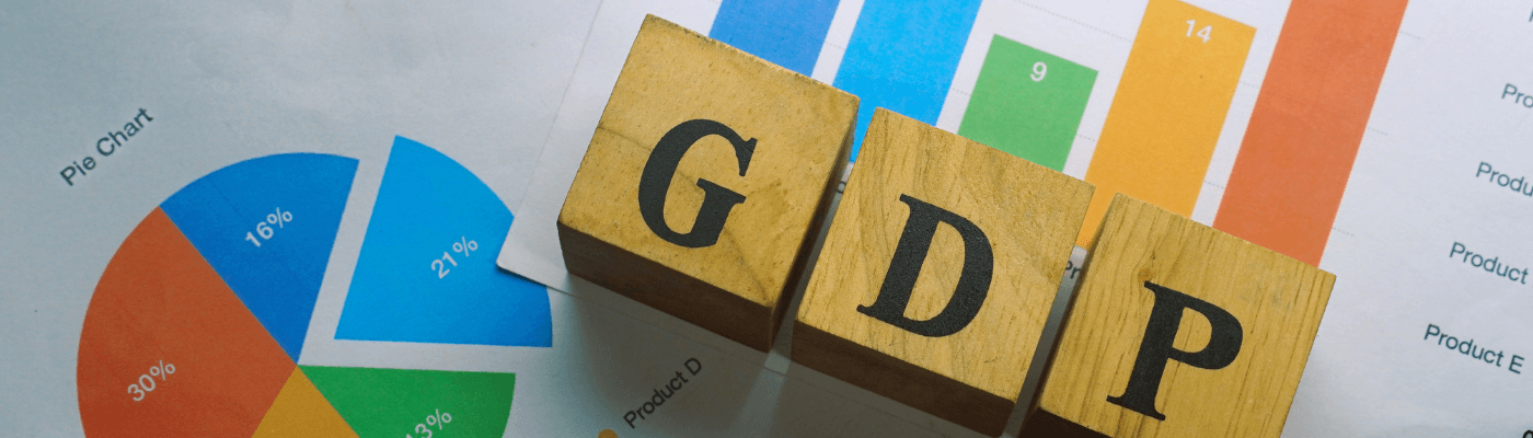 Three wooden letter blocks spelling "GDP" rest on top of colorful bar and pie charts, representing the measurement of gross domestic product.
