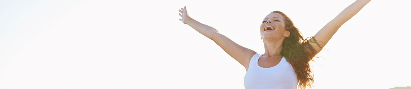 A young woman stands outdoors with her arms raised and eyes closed, smiling — representing the concept of quality of life and well-being that GDP alone cannot fully measure.