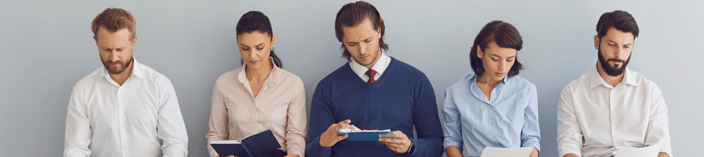Five people sitting in a row reading documents, representing job seekers in a waiting room — illustrating the concept of labor force participation and unemployment explored in this lesson.