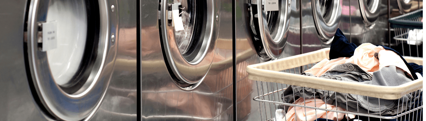 A row of industrial washing machines at a laundromat with a laundry basket in the foreground, representing the real-world tariff case study on U.S. washing machine imports explored in this lesson.