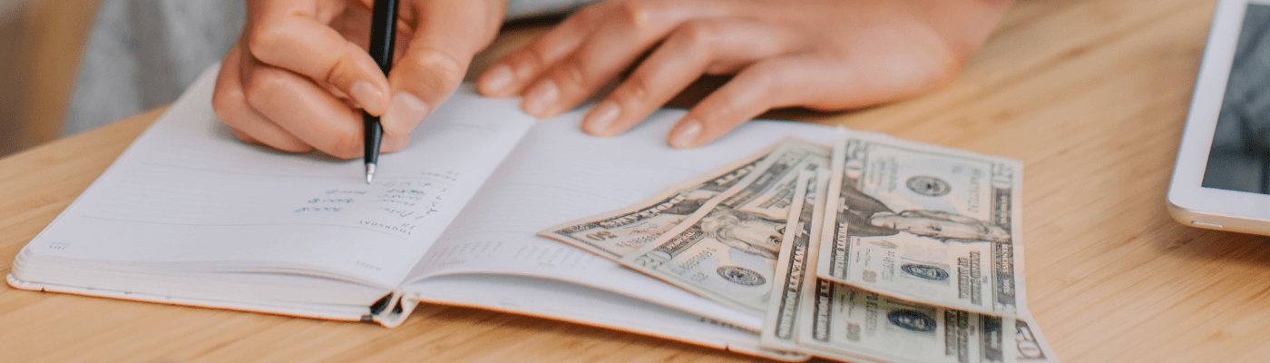 Tabletop with personal balance their cash and finances in a ledger.