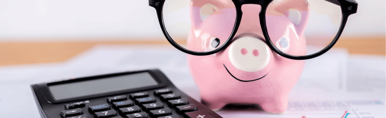 A piggy bank, wearing glasses, next to financial paperwork and a calculator. 