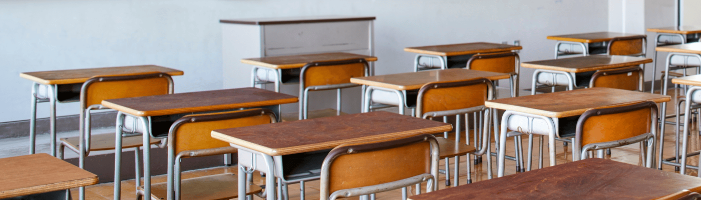 Rows of empty wooden student desks with metal frames in a bright classroom, representing investment in education as a driver of productivity and long-run economic growth.