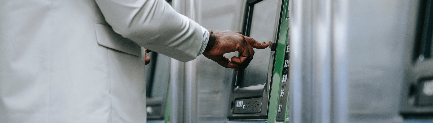 A person in a white suit using an ATM, with dollar amount options visible on the screen, illustrating how commercial banks serve as financial intermediaries between savers and borrowers.