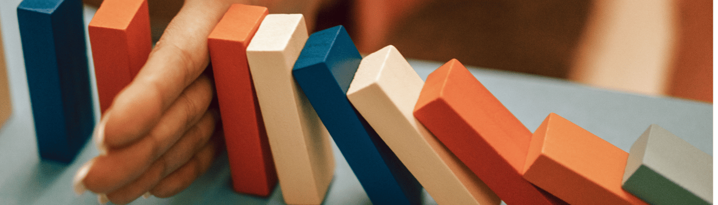 A hand stopping a row of colorful falling dominoes mid-collapse, representing how insurance protects against financial risk and shields individuals from a chain reaction of economic losses.
