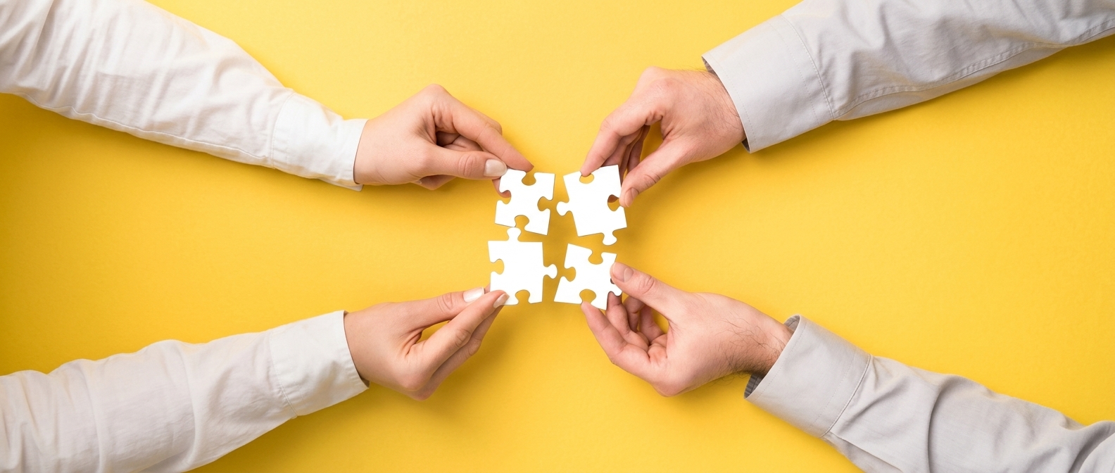 Two sets of hands hold four complementary puzzle pieces.