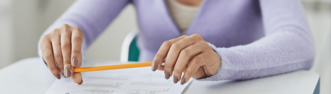 A student in a lavender sweater sits at a desk holding a pencil over a printed worksheet.
