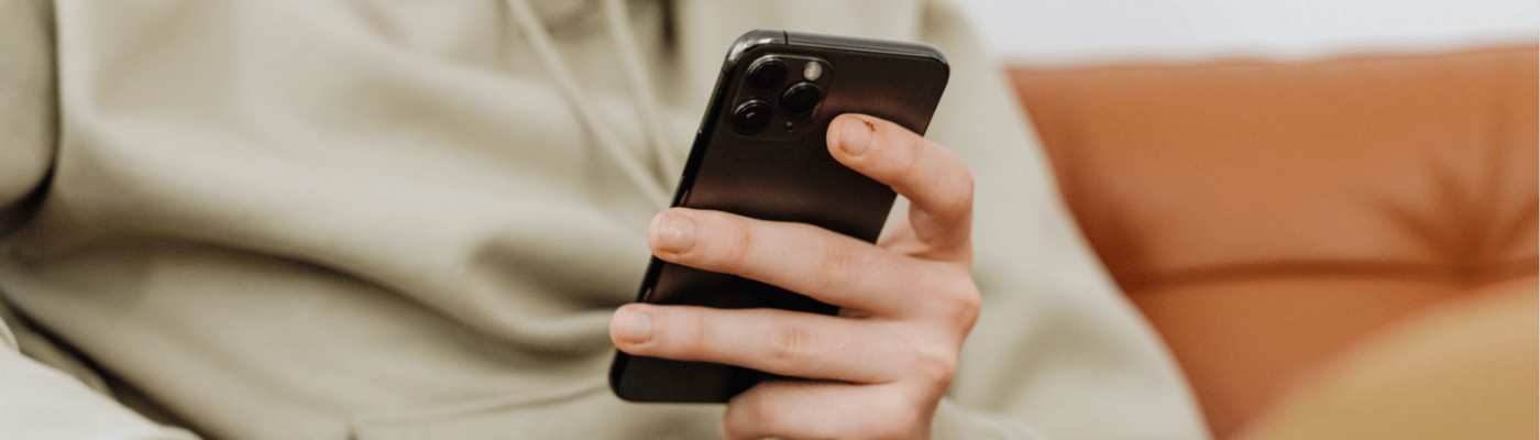 Hand holding a phone while person is seated on a couch.